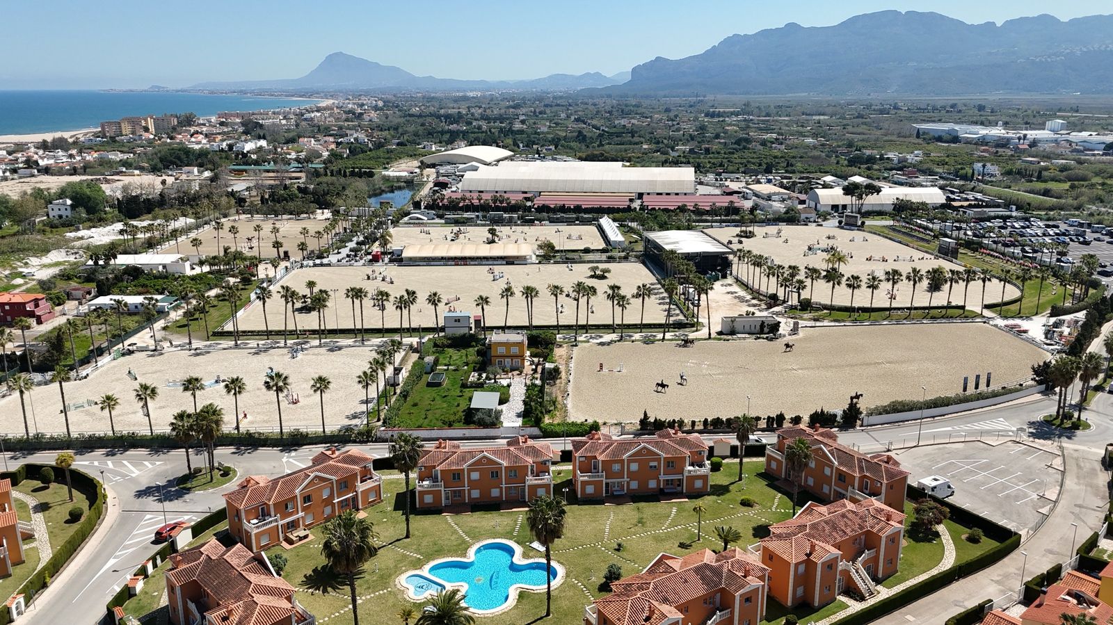 Vista aérea del centro ecuestre Oliva Nova con pistas de arena, palmeras y montañas al fondo